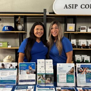 Osiris Rivas (Cultural and Linguistics Program Advisor) and Maria Colomer (Community Engagement Program Coordinator), standing behind outreach booth.