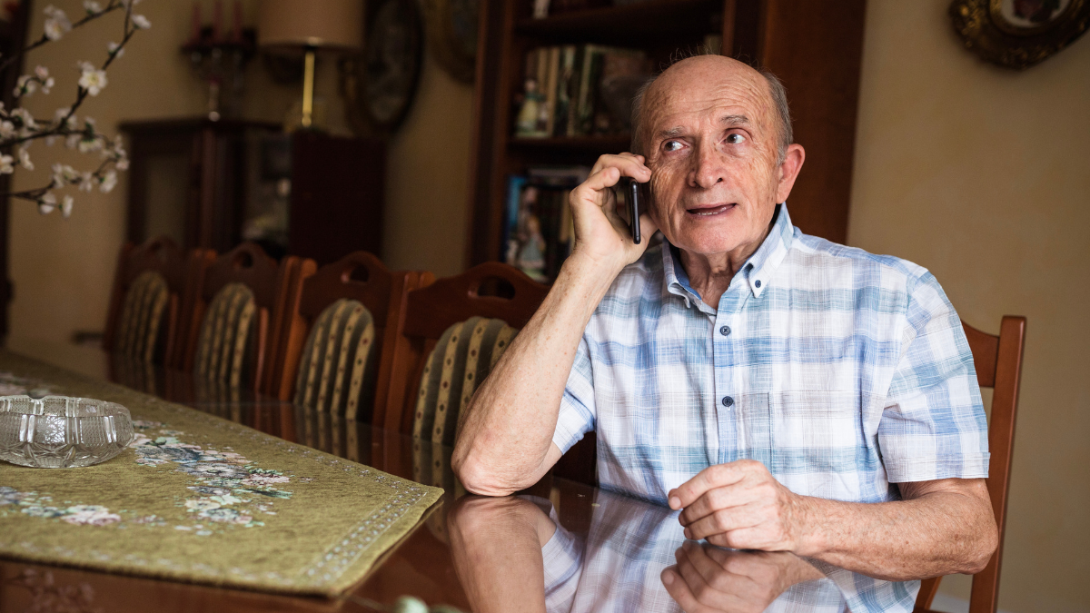 Un hombre mayor se sienta en la mesa del comedor hablando por teléfono celular