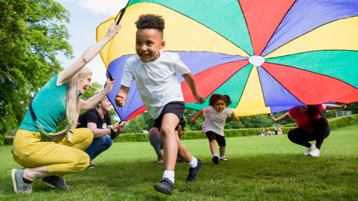 Boy running under a colorful parachute on a grassy field