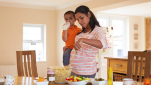 Pregnant mother holds toddler while cooking dinner.