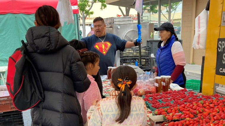 A family visits a stall at the farmer's market to get fresh food.