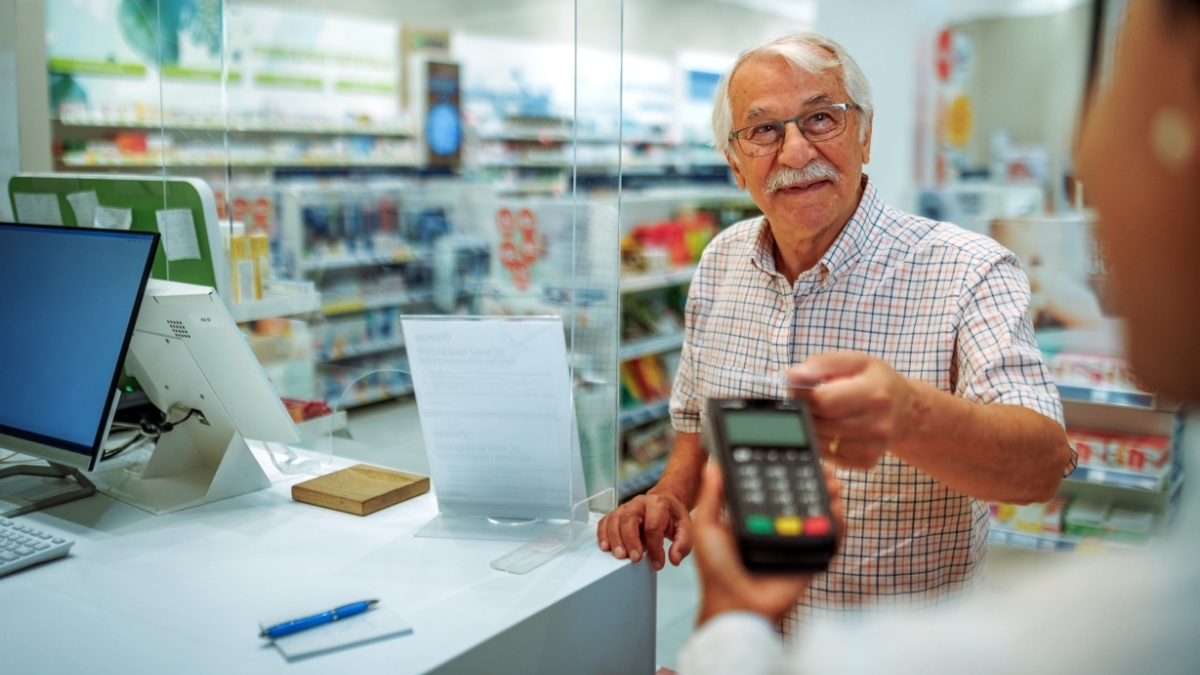 Un hombre mayor paga con tarjeta en la farmacia.