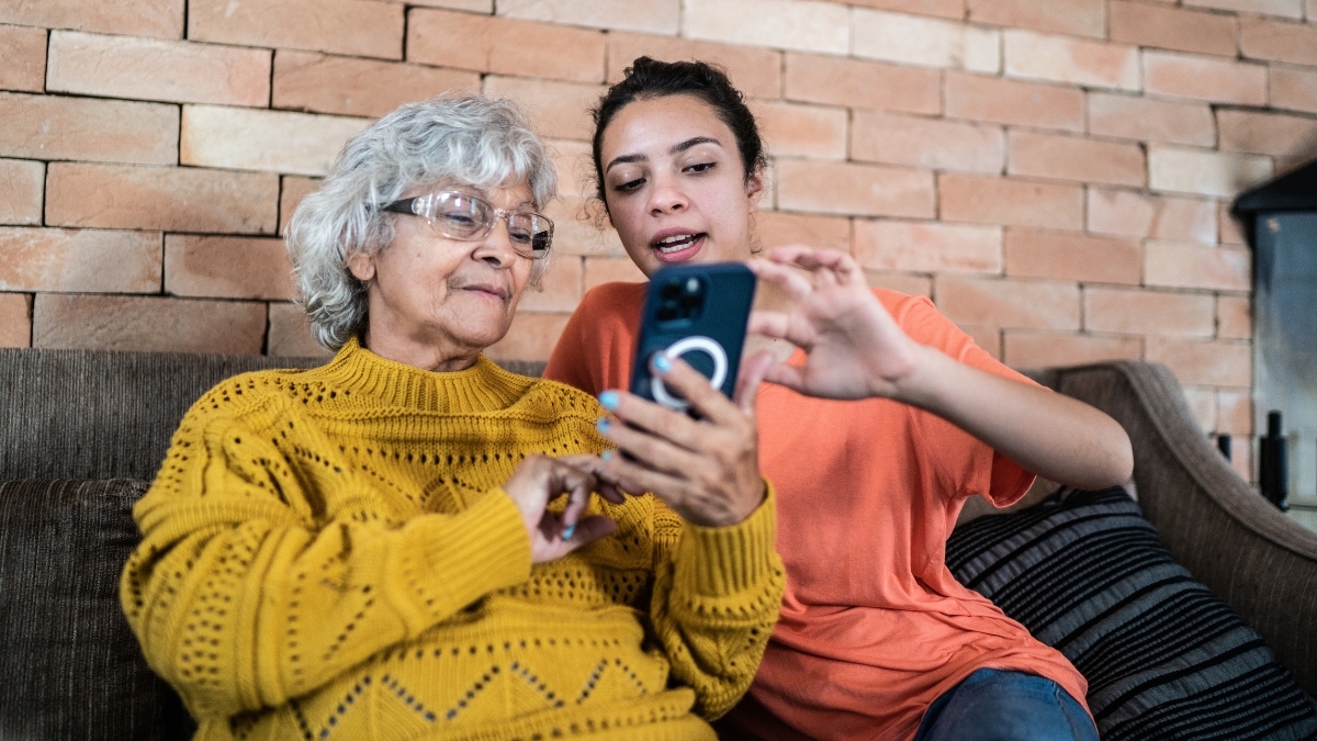 Una mujer mayor está sentada con una mujer más joven mientras revisan sus teléfonos.