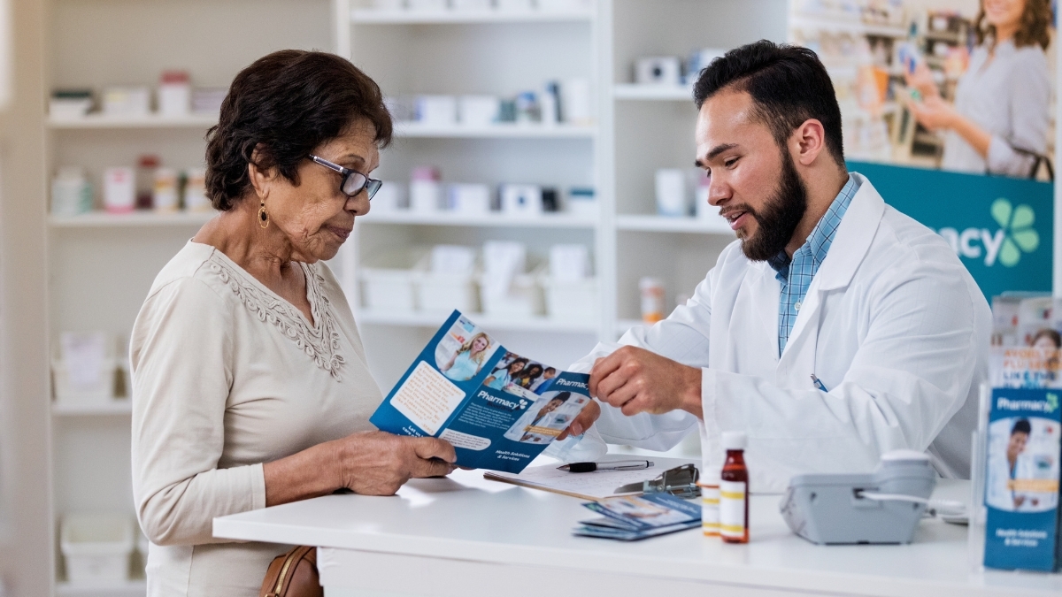 Un farmacéutico habla con una mujer mayor en la farmacia mientras le muestra un folleto.