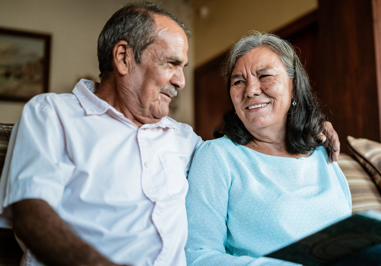 Married couple sitting on couch together smiling looing at each other.