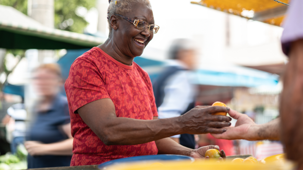 Image of outdoor produce vendor handing piece of fruit to customer