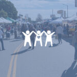 Street shot of outdoor farmer's market with lots of people in the frame and booths.