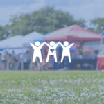 Pop-up tents on top of flowery grass at outdoor outreach event.