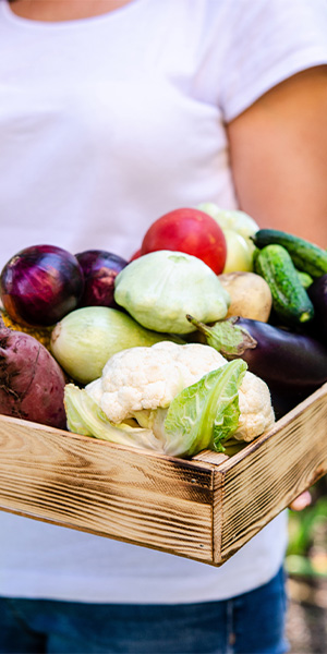 Человек держит коробку со свежими овощами.