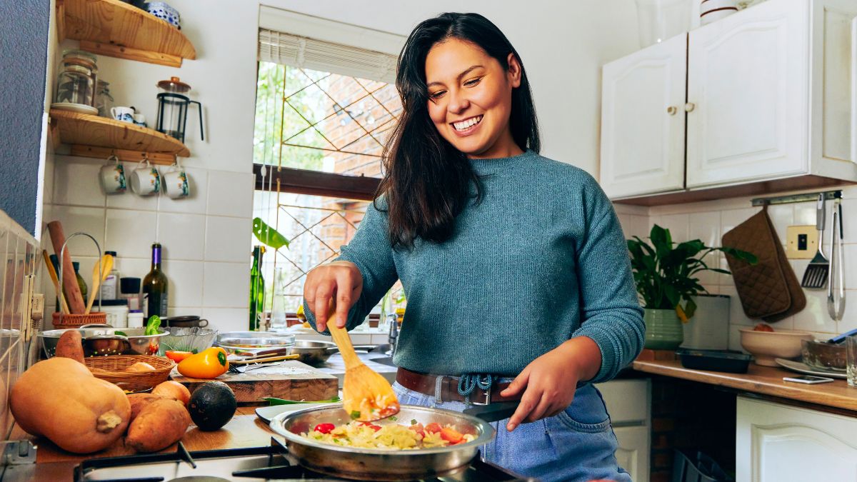 ਔਰਤ ਆਪਣੀ ਰਸੋਈ ਵਿੱਚ ਖਾਣਾ ਬਣਾਉਂਦੇ ਹੋਏ ਮੁਸਕਰਾਉਂਦੀ ਹੈ